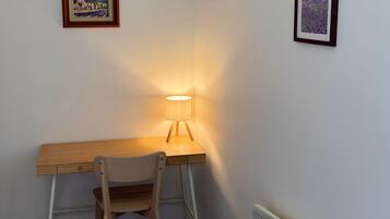 Een kamer met een houten bureau, een stoel, een wandlamp en twee ingekaderde foto's.
