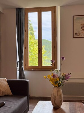A room with a window, a sofa, a table, and a vase with flowers. - La Fenêtre sur le Ventoux (Montbrun-les-Bains)