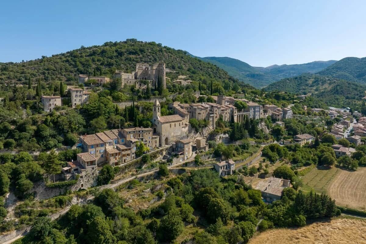 Ein Dorf an einem Hügel mit historischen Steinhäusern, terrassierten Feldern und einer markanten, burgenähnlichen Struktur.