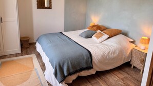 Une chambre à coucher comprenant un lit, des lampes de chevet, un miroir, une armoire et un petit tabouret.