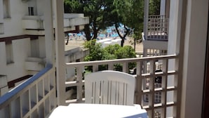 Ein Balkon mit weißem Tisch und Stuhl mit Blick auf einen Strand mit Sonnenschirmen und Bäumen.