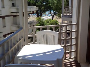 Ein Balkon mit weißem Tisch und Stuhl mit Blick auf einen Strand mit Sonnenschirmen und Bäumen.