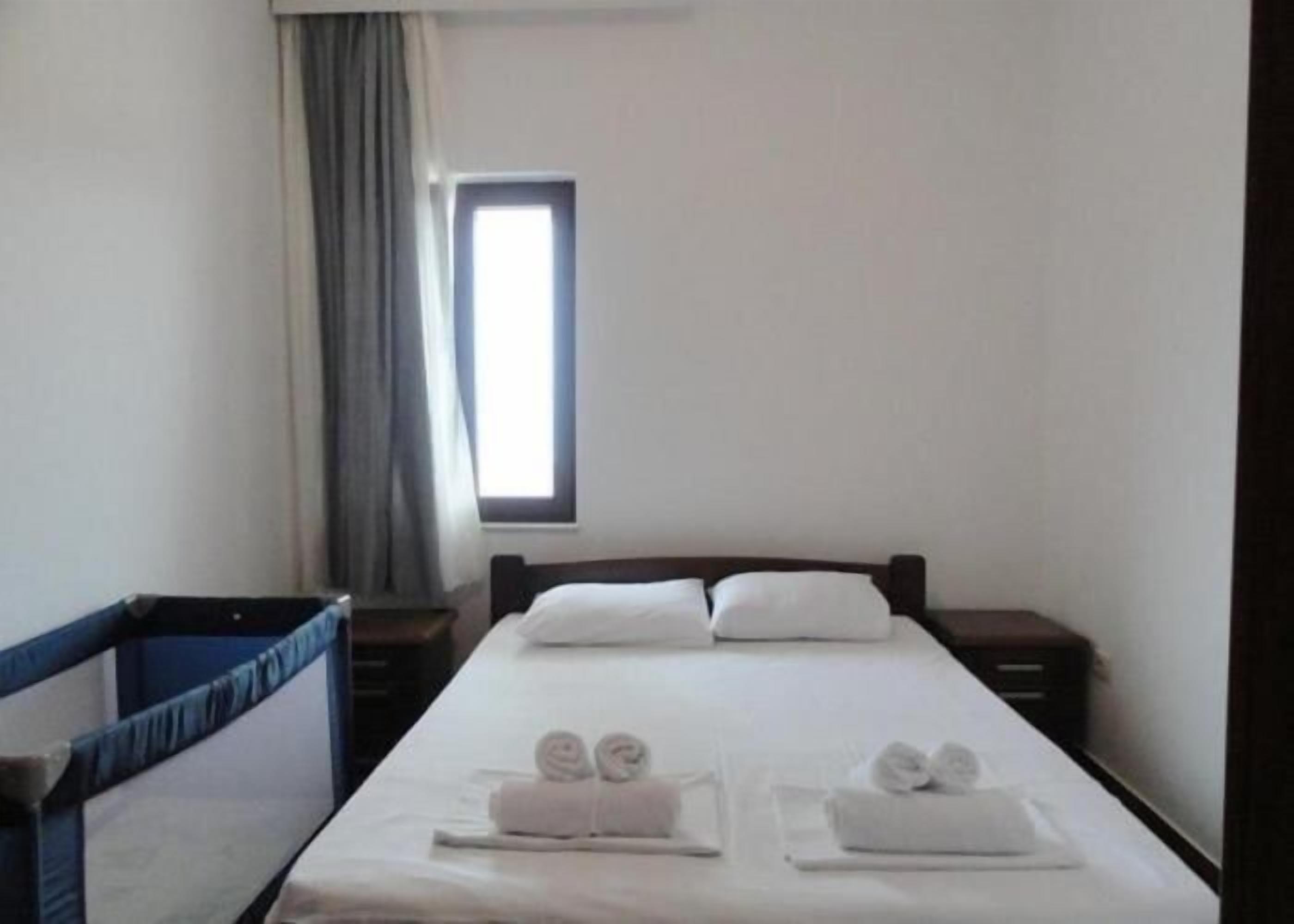 Une chambre d’hôtel avec un lit simple, une fenêtre, un rideau et une petite table avec des serviettes.
