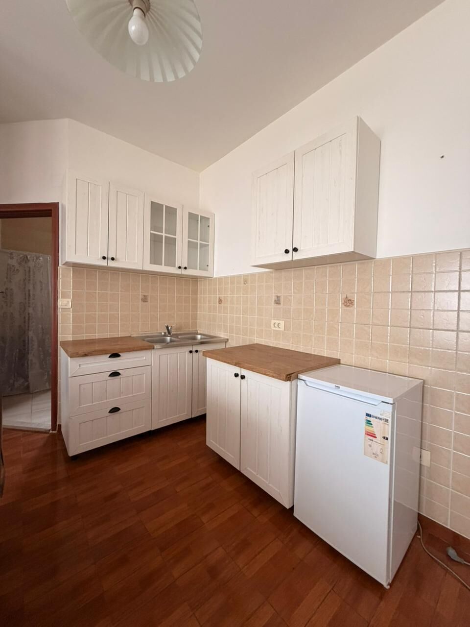 Una cocina con armarios blancos, encimera de madera y refrigerador blanco.