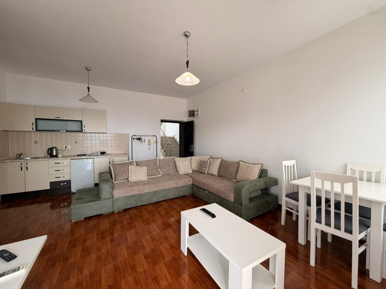 A modern living room with a sectional sofa, a dining table with chairs, a white coffee table, and a kitchen area with cabinets and a sink.