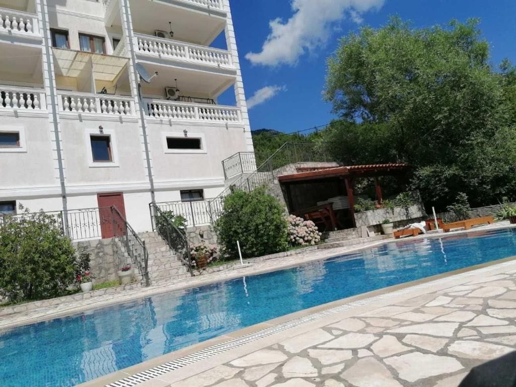 A swimming pool with a stone deck, a multi-story building with balconies, and a small covered area with seating.