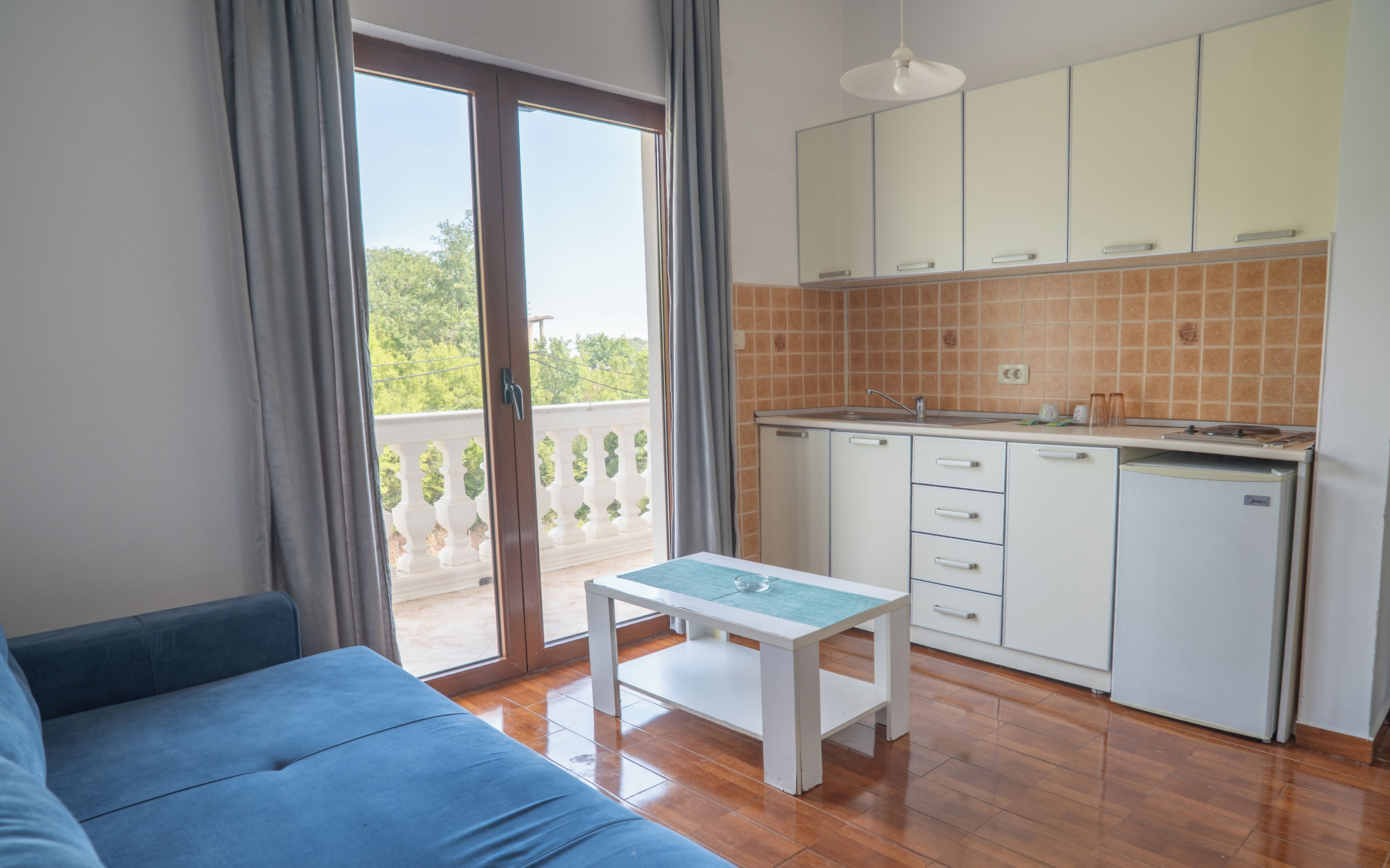 Eine moderne Küche mit weißen Schränken, einem eingebauten Backofen und einem Spülbecken. Ein kleiner Esstisch mit blauer Tischdecke steht daneben.