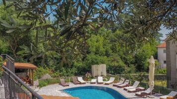 Une piscine avec des chaises longues, une terrasse en bois et un chemin en pierre.