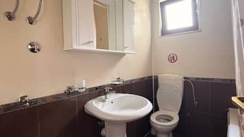 A bathroom with a pedestal sink, a toilet, a mirror, and a window.
