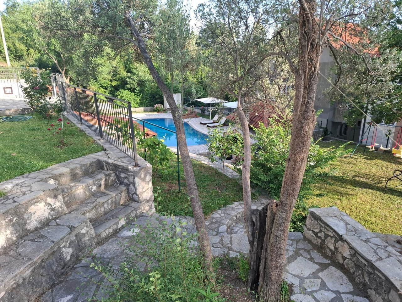 Un escalier en pierre mène à une piscine entourée d’arbres et bordée d’une pelouse.