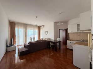 A modern living room with a sofa, dining table, and kitchen area. - Apartments Oasis (Markovići)