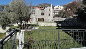 A stone building with a balcony, surrounded by a stone wall and a metal fence. - Apartments Oasis (Markovići)