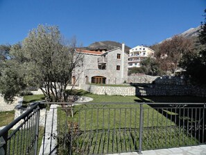 A stone building with a balcony, surrounded by a stone wall and a metal fence. - Apartments Oasis (Markovići)
