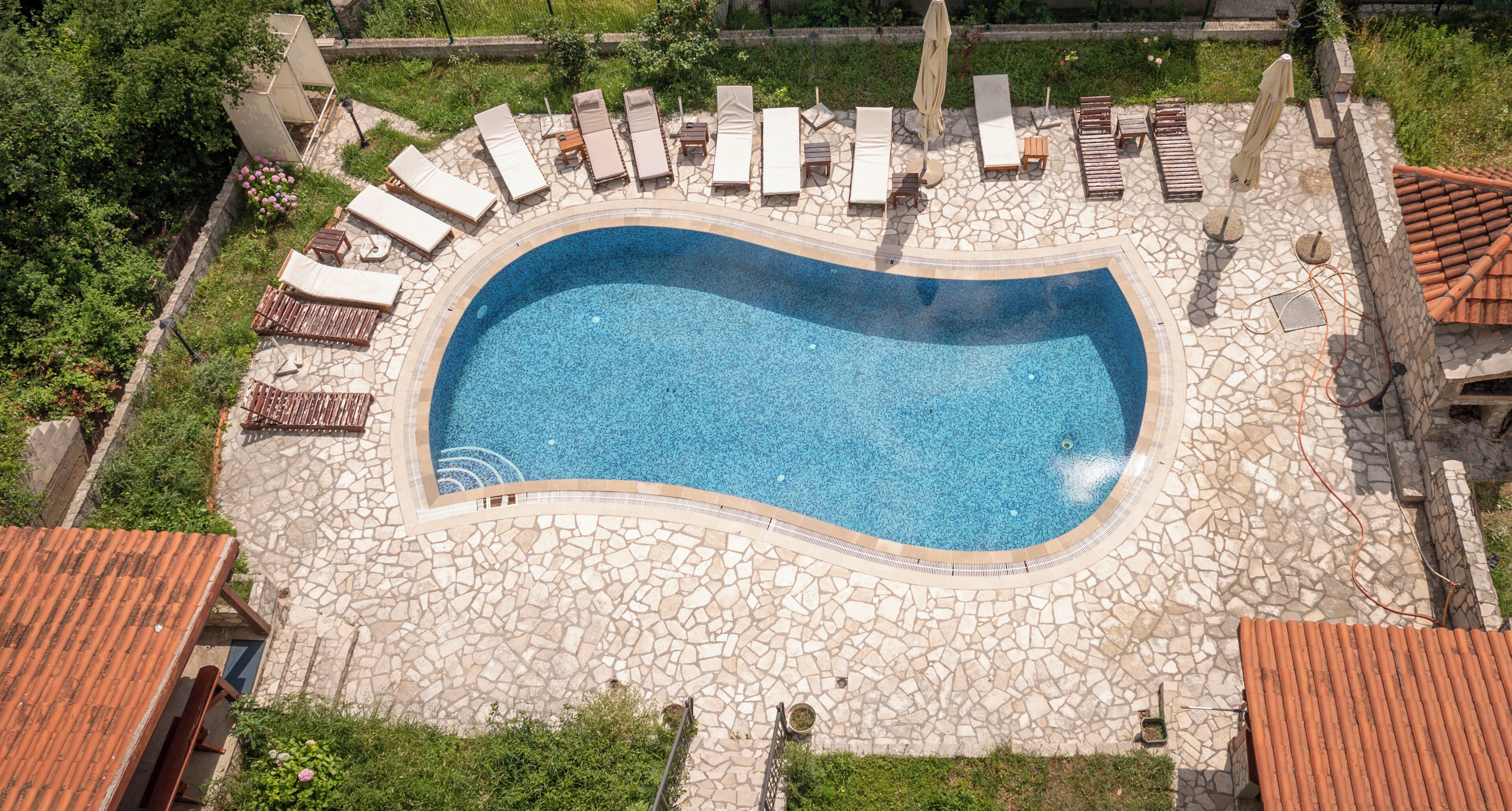 Vue aérienne d’une piscine avec des chaises longues et une terrasse en pierre.