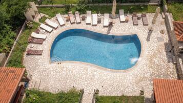 Vue aérienne d’une piscine avec des chaises longues et une terrasse en pierre.