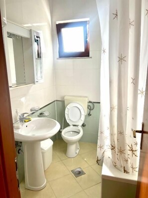 Une salle de bain avec un lavabo sur colonne, des toilettes et une fenêtre située au-dessus des toilettes.