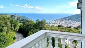 A balcony with a white balustrade overlooking a coastal cityscape and the sea. - Apartments Oasis (Markovići)
