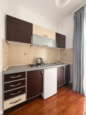 A compact kitchen with a refrigerator, a kettle, and a sink.