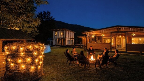 A group of people around a fire pit in a grassy area with a house in the background. - River side and near forest chalet in Brad/Ribita perfect for a relaxing getaway. (Brad)