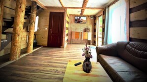 A log cabin interior with a wooden floor, a sofa, a remote control, and a vase with flowers on a coffee table. - River side and near forest chalet in Brad/Ribita perfect for a relaxing getaway. (Brad)
