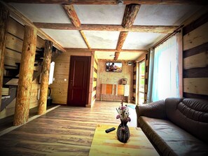 LâintĂ©rieur dâune cabane en rondins, avec un plancher en bois, un canapĂ©, une tĂ©lĂ©commande et un vase rempli de fleurs posĂ© sur une table basse.
