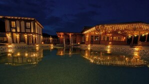 A nighttime view of a hotel with a swimming pool, illuminated by string lights, and a reflection in the water. - River side and near forest chalet in Brad/Ribita perfect for a relaxing getaway. (Brad)