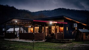 A rustic building with a covered outdoor seating area, a visible air conditioning unit, and a wooden deck. - River side and near forest chalet in Brad/Ribita perfect for a relaxing getaway. (Brad)