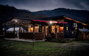 A rustic building with a covered outdoor seating area, a visible air conditioning unit, and a wooden deck. - River side and near forest chalet in Brad/Ribita perfect for a relaxing getaway. (Brad)