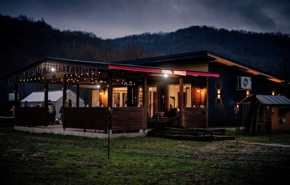 Un bĂątiment de style rustique dotĂ© dâun espace extĂ©rieur couvert avec des siĂšges, dâun appareil de climatisation visible et dâune terrasse en bois.