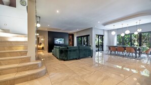 A spacious living area with a green sofa, a dining table with chairs, and a TV mounted on the wall. - Ultra-Luxury 4-Bedroom en-suite self catering Villa in Zimbali Coastal Resort (Ballito)