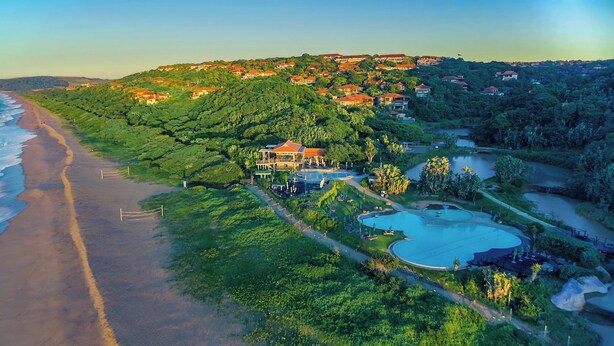 An aerial view of a coastal resort with a large swimming pool, lush greenery, and beachfront properties. - Ultra-Luxury 4-Bedroom en-suite self catering Villa in Zimbali Coastal Resort (Ballito)