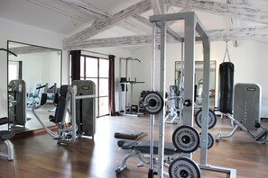 Ein Fitnessraum mit unterschiedlichen Trainingsgeräten, einer Bank und einem Boxsack.