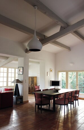 Ein geräumiger Essbereich mit hoher Decke, freiliegenden Balken, einem Esstisch mit Stühlen, einem Fernseher und einem Fenster, das für natürliches Licht sorgt.