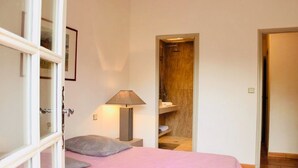 Ein Schlafzimmer mit einem Bett, einer Nachttischlampe, einer Tür zu einem Badezimmer und einem kleinen Regal mit Handtüchern.
