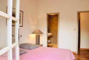 Ein Schlafzimmer mit einem Bett, einer Nachttischlampe, einer Tür zu einem Badezimmer und einem kleinen Regal mit Handtüchern.