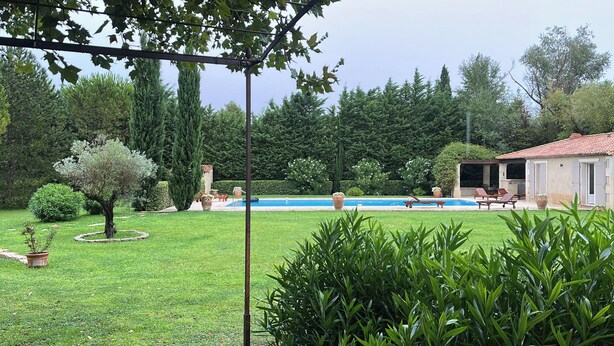Ein Pool mit Garten, ein überdachter Bereich mit Sitzgelegenheiten und ein Gebäude mit Ziegeldach.