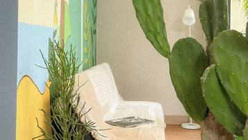A room with a cactus plant, a white chair, and a wall mural.