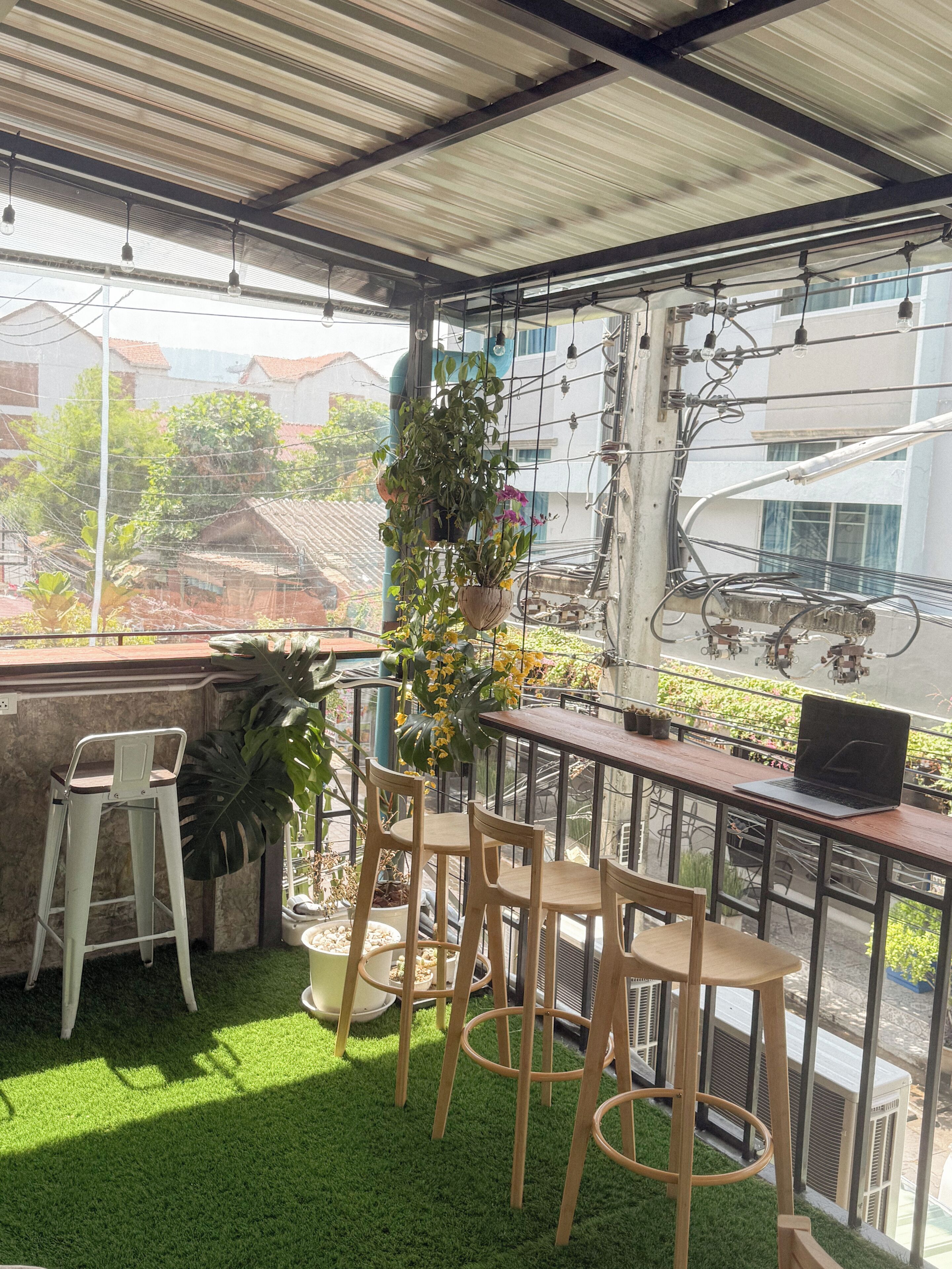 A covered outdoor seating area with artificial grass, wooden chairs, a table with a laptop, and potted plants.