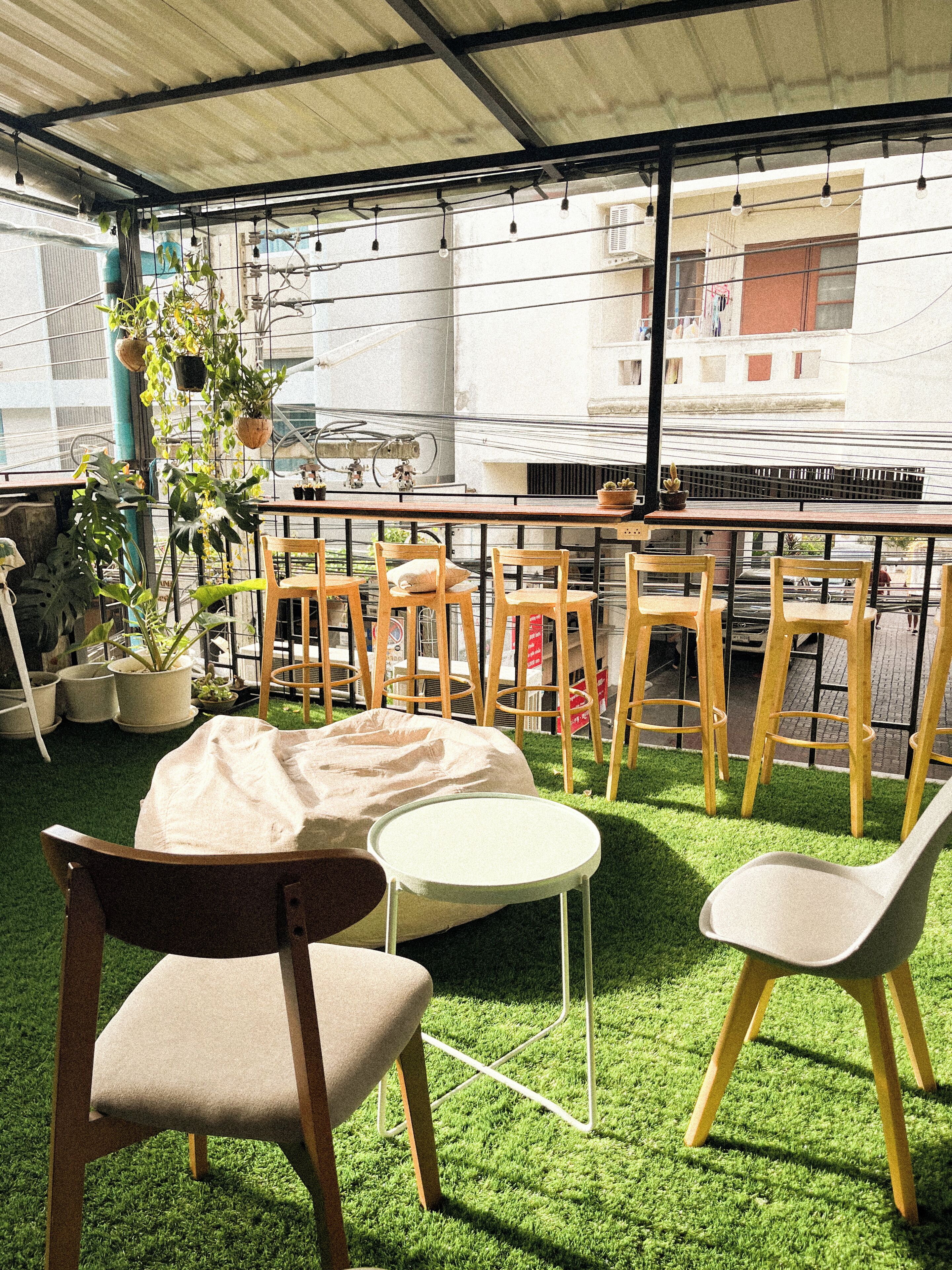 A rooftop terrace with artificial grass, wooden chairs, a small round table, and potted plants.