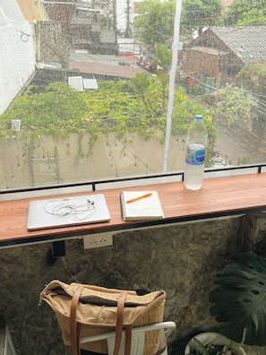 A window view of a residential area with a water bottle on the ledge, a notebook, and a pair of glasses on the table. - Basecamp Hostel (Chiang Mai)