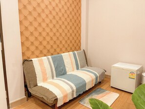 A small living area with a sofa, a refrigerator, and a wooden floor.