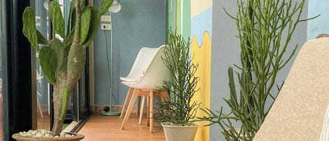 A room with a laptop on a couch, a potted plant, a chair, and a wall with a colorful mural.