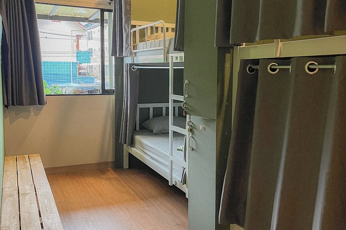 A bunk bed room with a window, a table, and a curtain.
