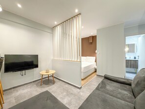 A modern hotel room with a flat-screen TV, a small round table, a bed with a wooden headboard, and a grey sofa. - SmartLiving Central Apt 1 (Thessaloniki)