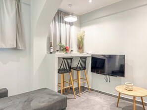 Une cuisine moderne équipée d’un téléviseur, de deux tabourets de bar, d’une petite table ronde et d’un canapé gris.