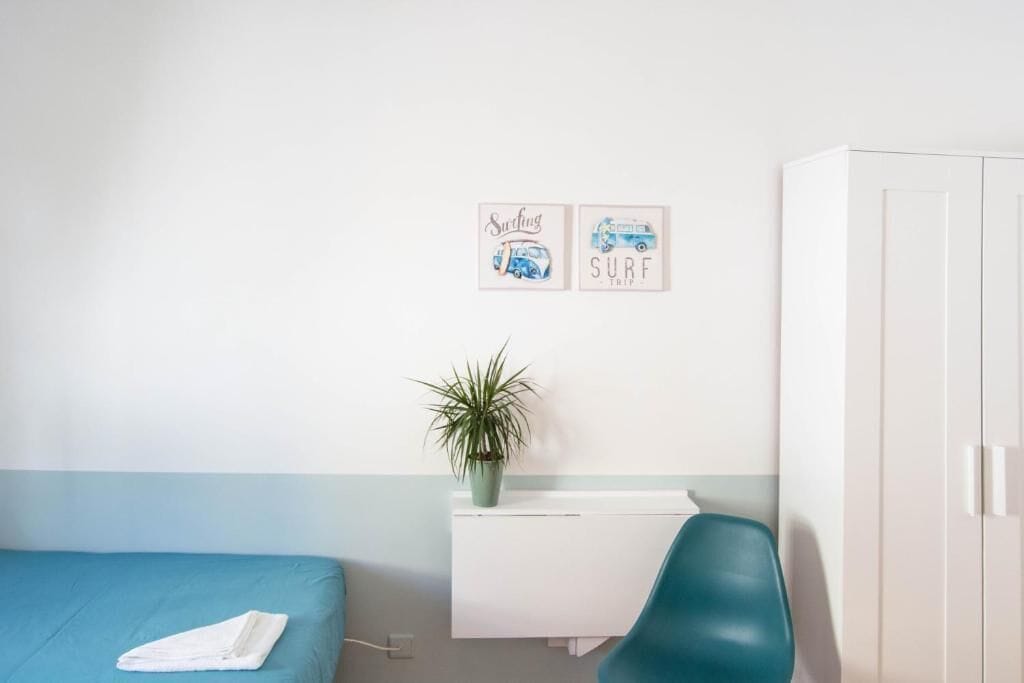 A bedroom with a bed, a desk, a chair, a wardrobe, and two wall decorations.