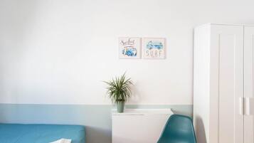 A bedroom with a bed, a desk, a chair, a wardrobe, and two wall decorations.