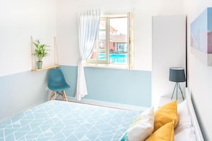 A bedroom with a bed, a window with curtains, a chair, a plant, and a lamp. - OLA Guesthouse (ESMORIZ)