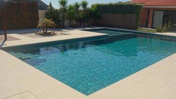 Una piscina rectangular con agua azul cristalina, rodeada por un suelo de baldosas y una valla de madera.