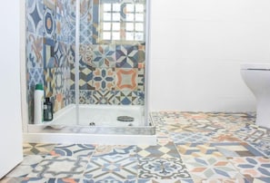 A bathroom with a shower area, tiled walls, and a patterned floor. - OLA Guesthouse (ESMORIZ)